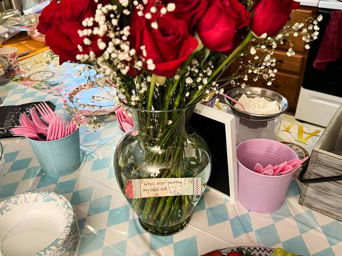 a vase of red roses with a sign on it that says "who's been painting the roses red?"