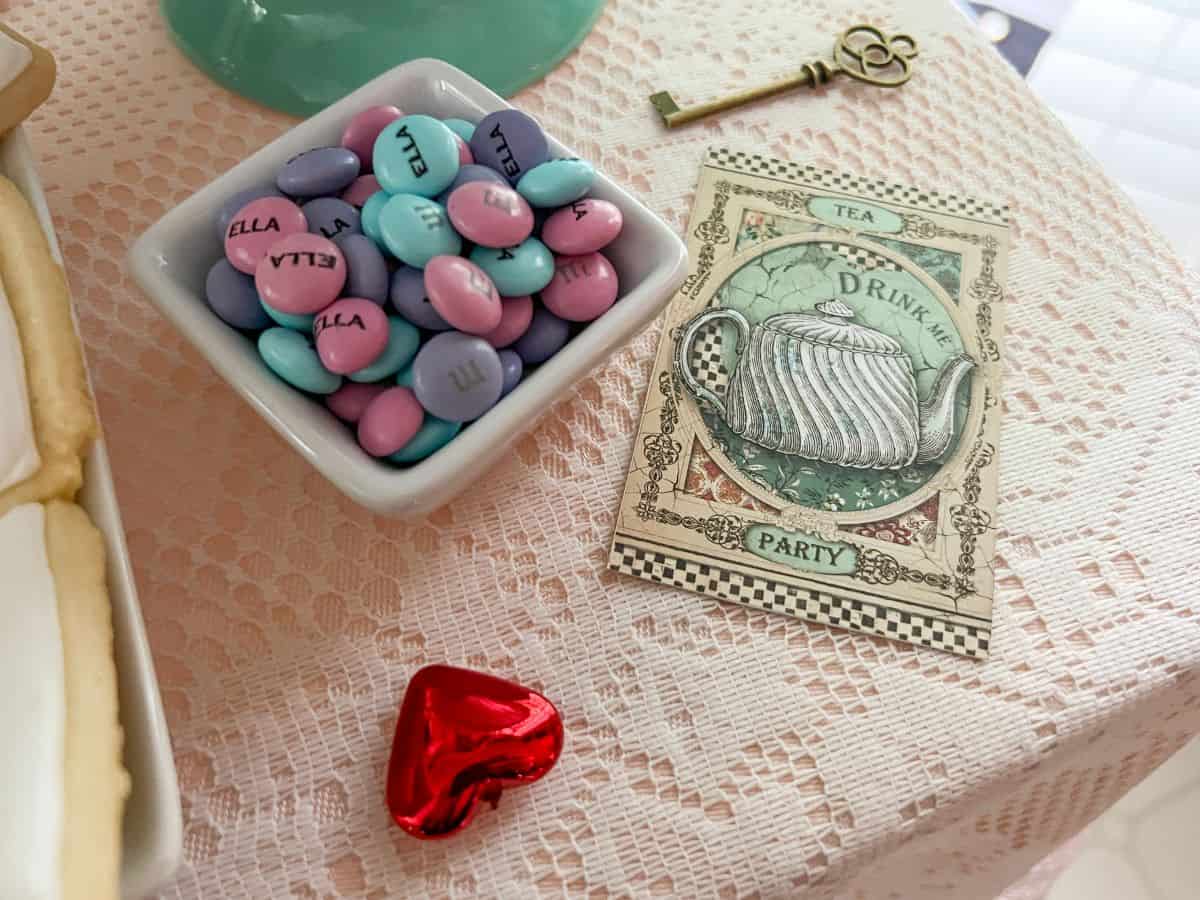 a dish of M&M's next to a vintage Alice in Wonderland card with a brass key