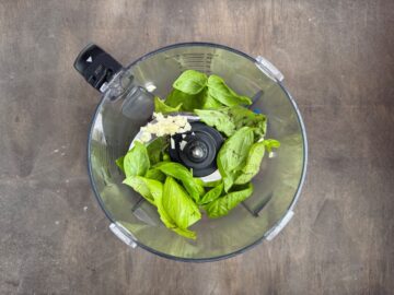 basil leaves and garlic in the bowl of a food processor