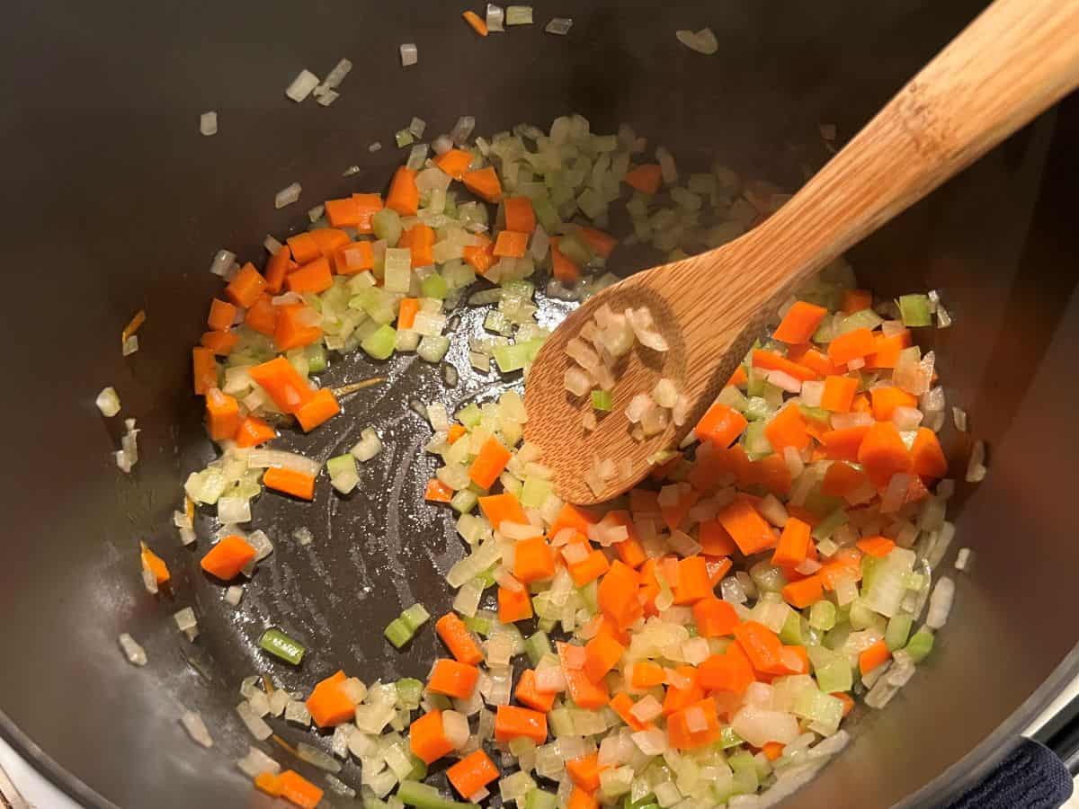 celery, carrots and onion sauteing in a stock pot with a wooden spoon