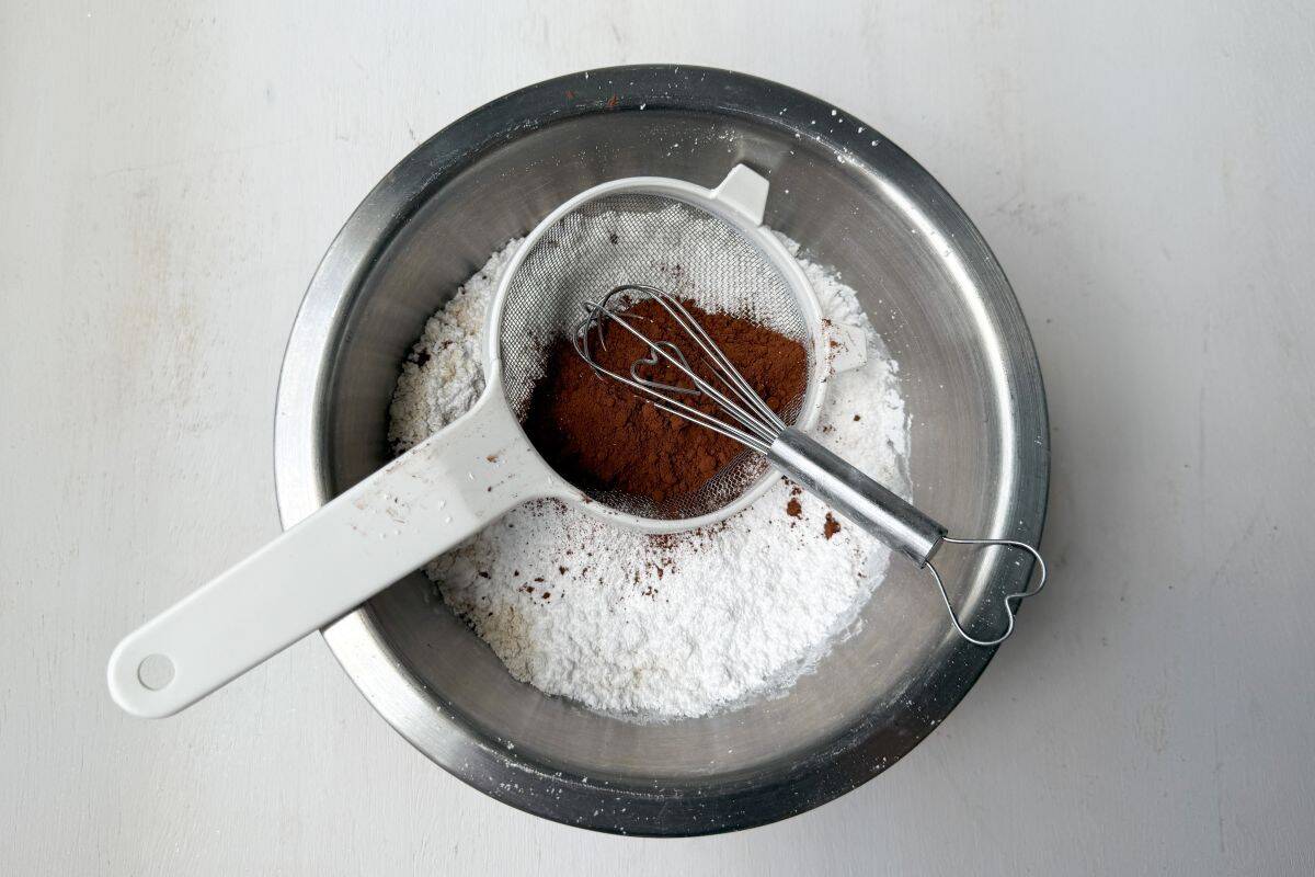 cocoa powder in a small mesh sifter with a small whisk over a bowl of white dry ingredients