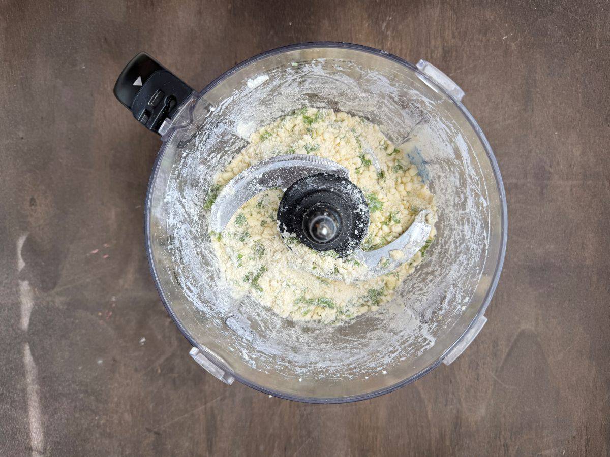 basil garlic tart dough being mixed in the bowl of a food processor