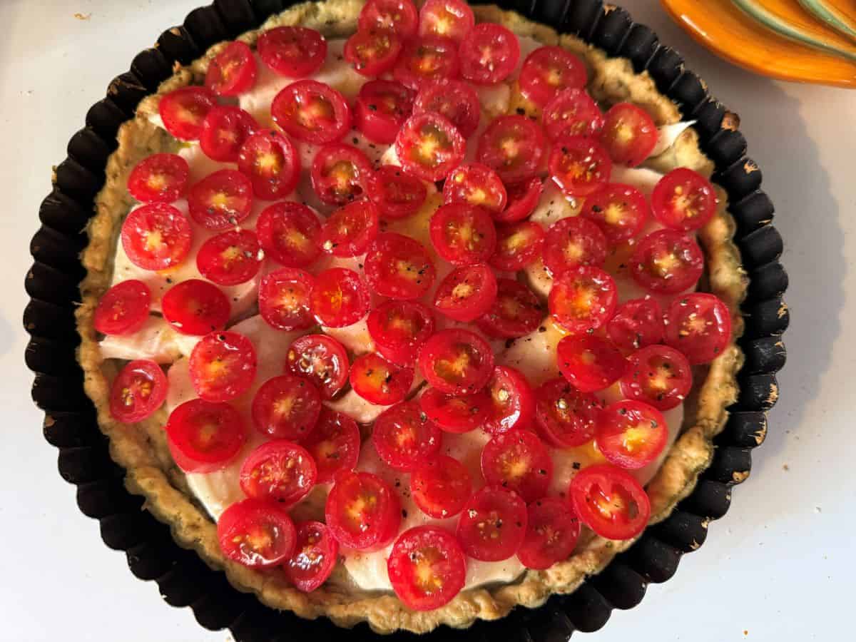 a tart pan filled with crust, cheese and sliced cherry tomatoes on top