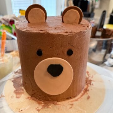 a teddy bear cake on a cake board with waxed paper pieces under the cake to protect the cake board