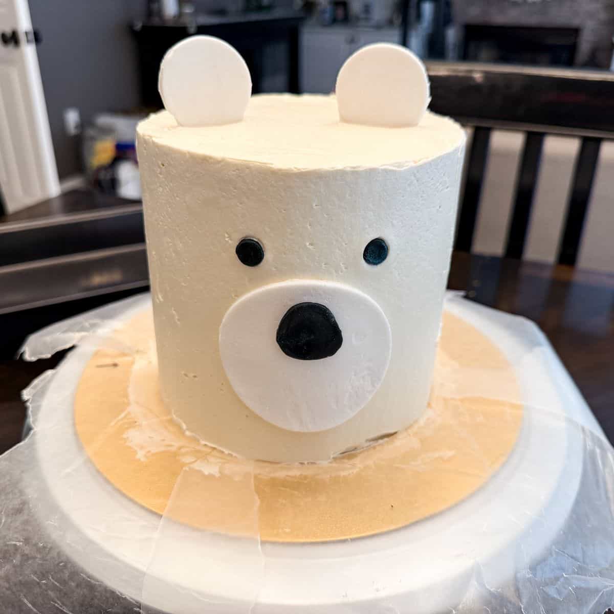 a polar bear cake on a cake board with waxed paper pieces under the cake to protect the cake board
