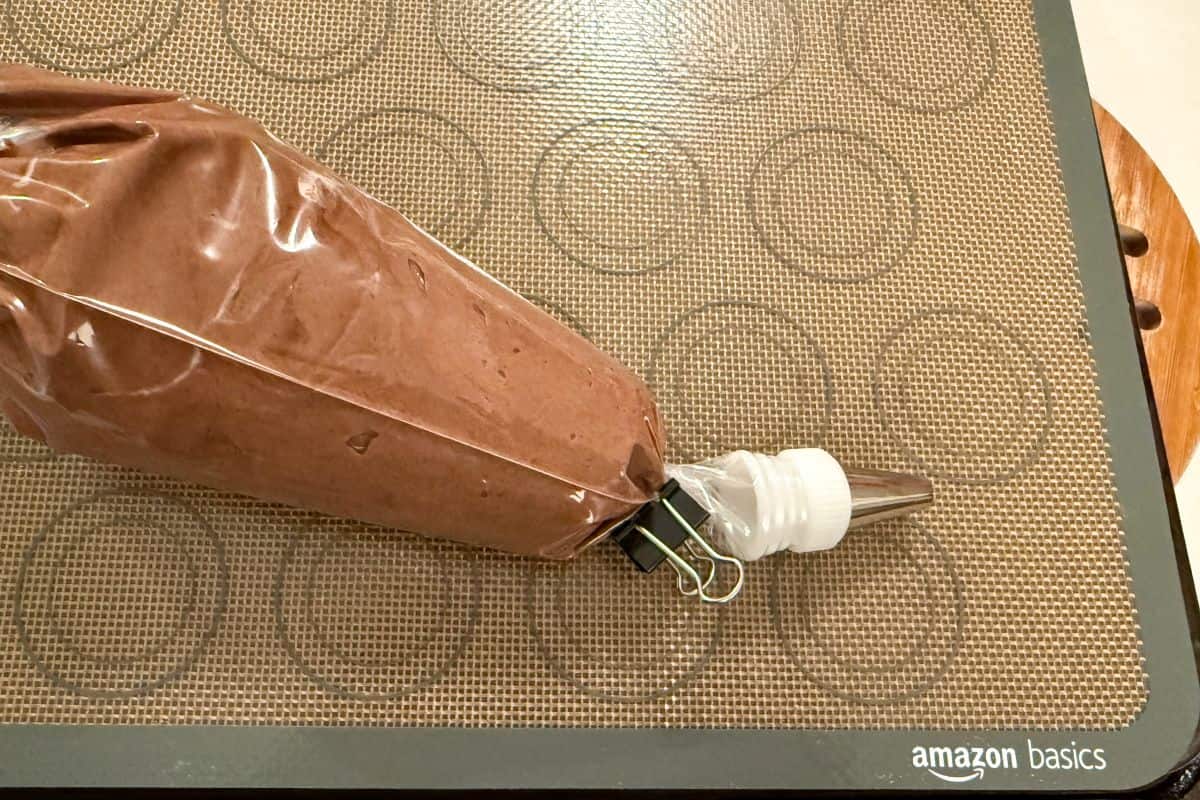 chocolate macaron batter in a piping bag sealed with a binder clip on top of a macaron mat