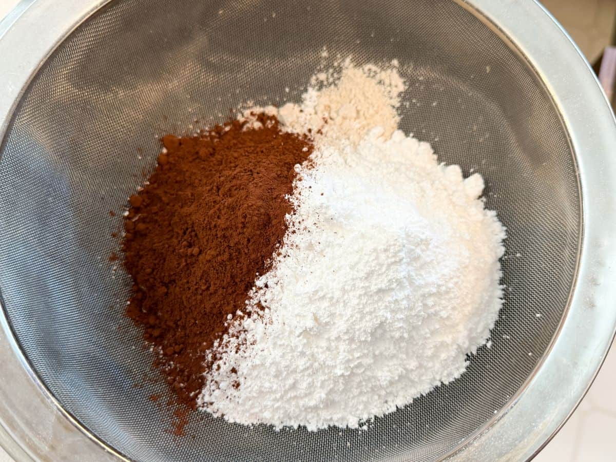 sifted cocoa powder on the left side of a bowl with white dry ingredients on the right