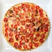 a tomato mozzarella tart with garlic basil crust on a white plate