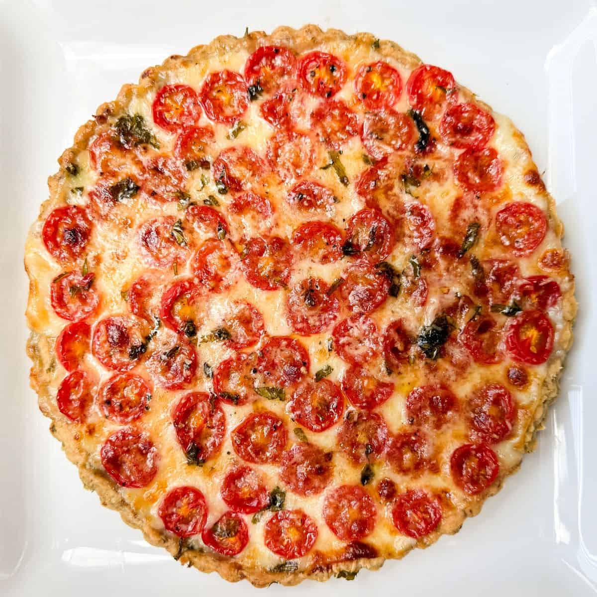 a tomato mozzarella tart with garlic basil crust on a white plate