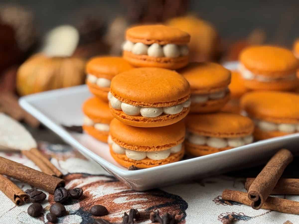 Nut Free Pumpkin Spice Latte Macarons on a white plate with cinnamon sticks and cloves around it