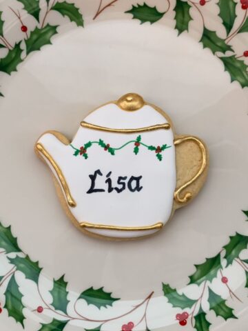 a personalized holly teapot sugar cookie on a holly bordered plate