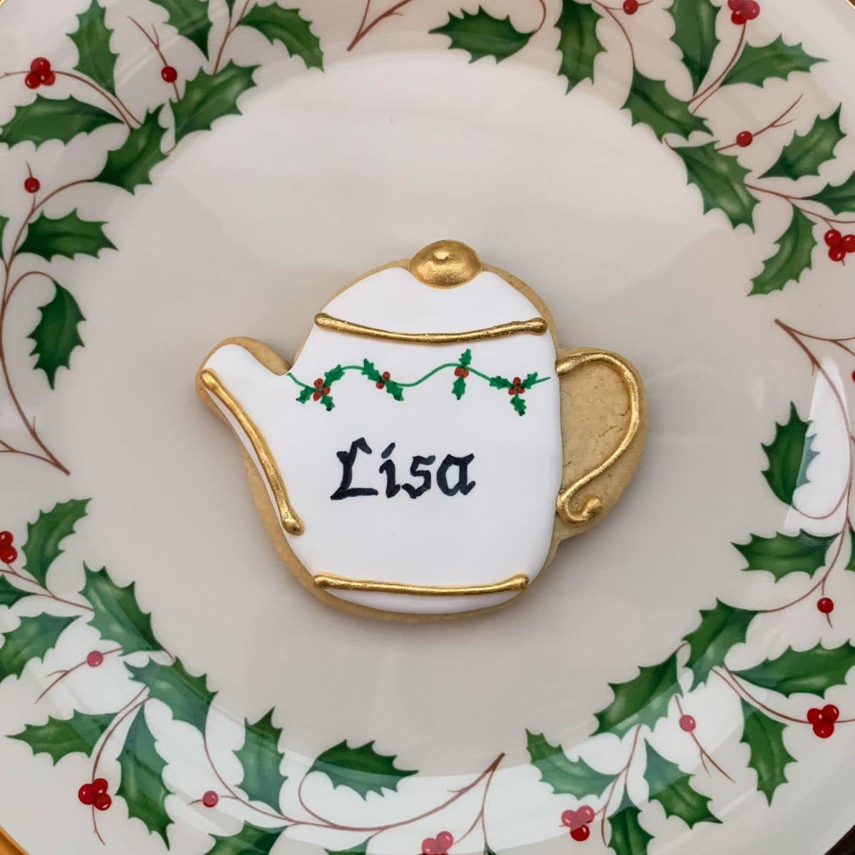 a personalized holly teapot sugar cookie on a holly bordered plate