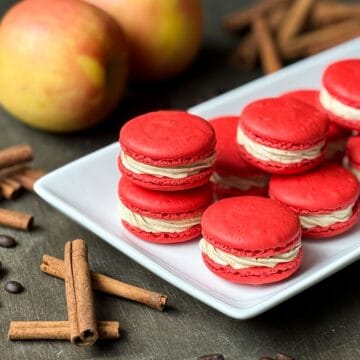 Nut Free Apple Macchiato Macarons on a white platter with apples and cinnamon sticks around it