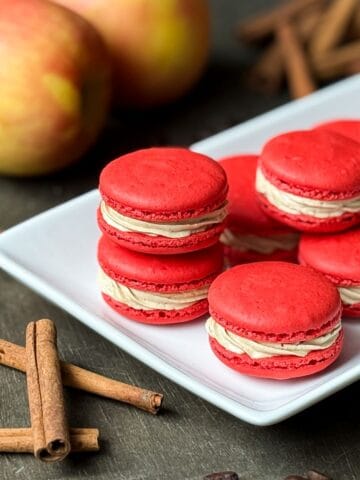 Nut Free Apple Macchiato Macarons on a white platter with apples and cinnamon sticks around it