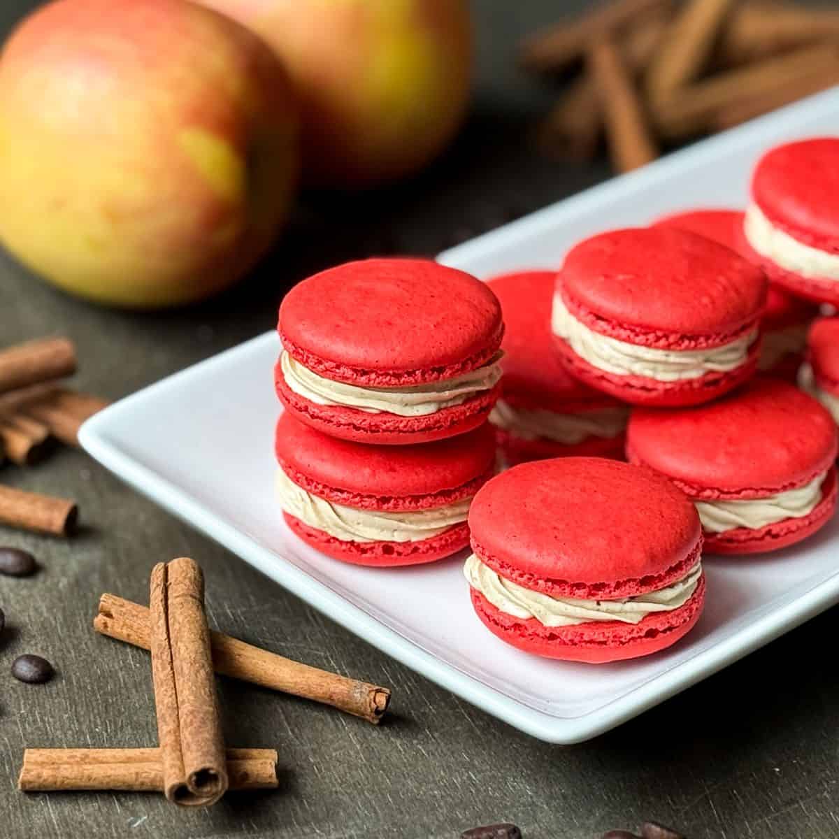 Nut Free Apple Macchiato Macarons on a white platter with apples and cinnamon sticks around it