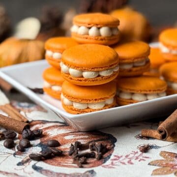Nut Free Pumpkin Spice Latte Macarons on a white plate with cinnamon sticks and cloves around it