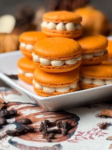 Nut Free Pumpkin Spice Latte Macarons on a white plate with cinnamon sticks and cloves around it