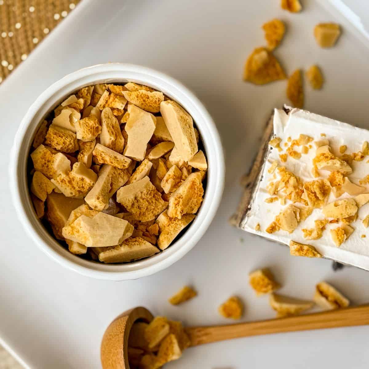 overhead photo of a ramekin filled with coffee crunch candy next to a piece of ice cream cake