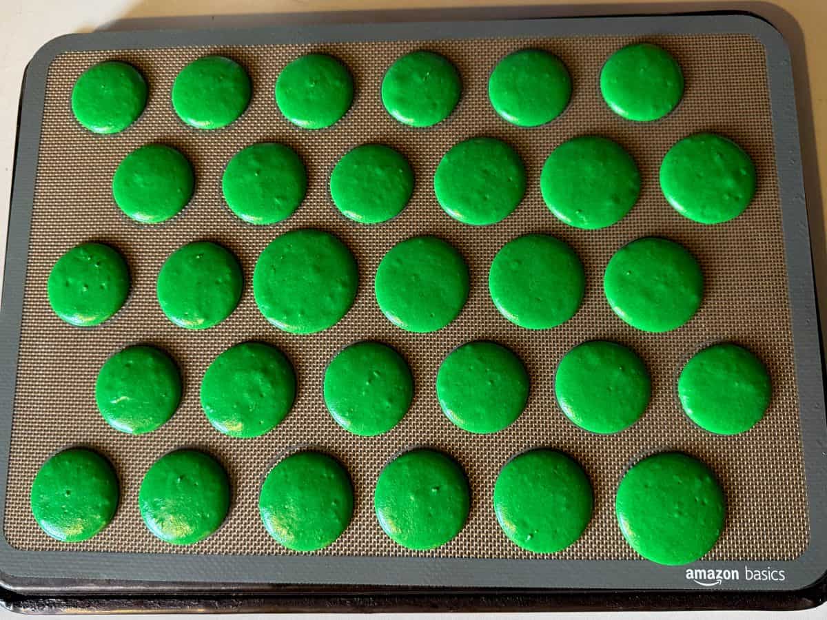 green macaron batter piped into 1-inch circle on a macaron mat