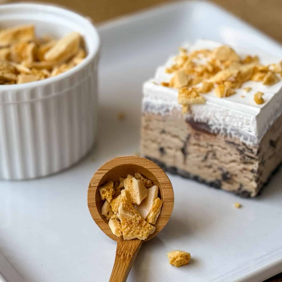 coffee crunch candy in a small wooden ladle next to a piece of ice cream cake and a ramekin filled with crunch candy