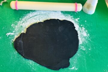 black fondant rolled out on a green mat with a small fondant rolling pin