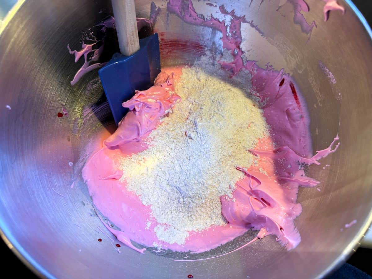 dry ingredients being incorporated into a bowl of pink meringue