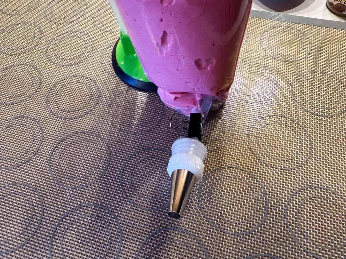 pink macaron batter in a disposable piping bag fitted with a medium round tip