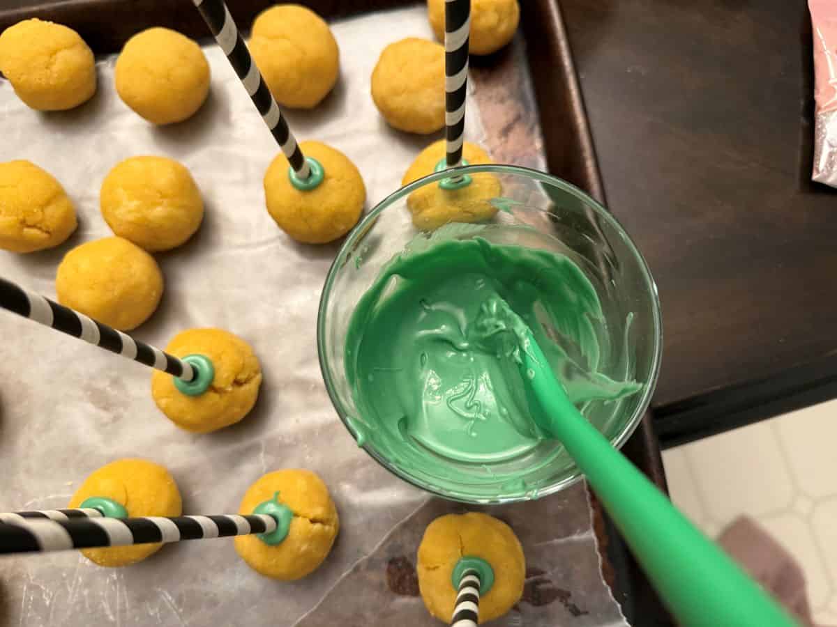 green candy melts melted in a glass with a green silicone spatula next to cake pops