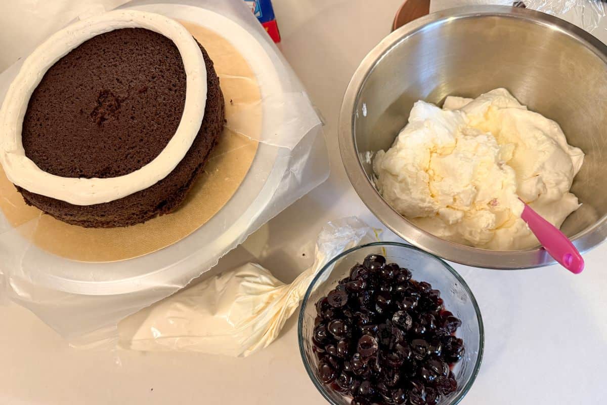 a layer of chocolate cake with a vanilla buttercream buttercream dam piped around the top on a gold cake board placed on a spinning cake stand