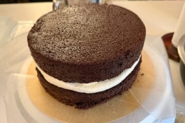 a second chocolate cake layer stacked on top of a cake assembled on a cake board