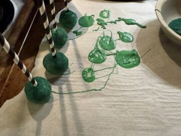 green cake pops on parchment paper with melted candy melt puddles