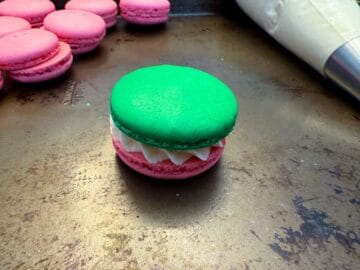 a green macaron shell on top of a pink shell with buttercream in the middle