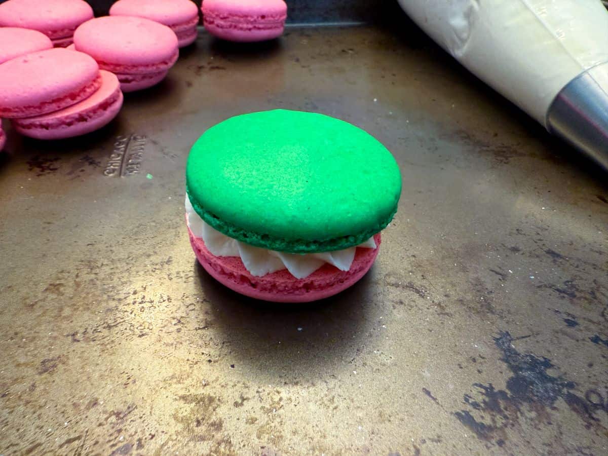 a green macaron shell on top of a pink shell with buttercream in the middle