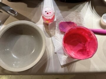 melted pink candy melts in a glass next to a bowl and a container of sanding sugar