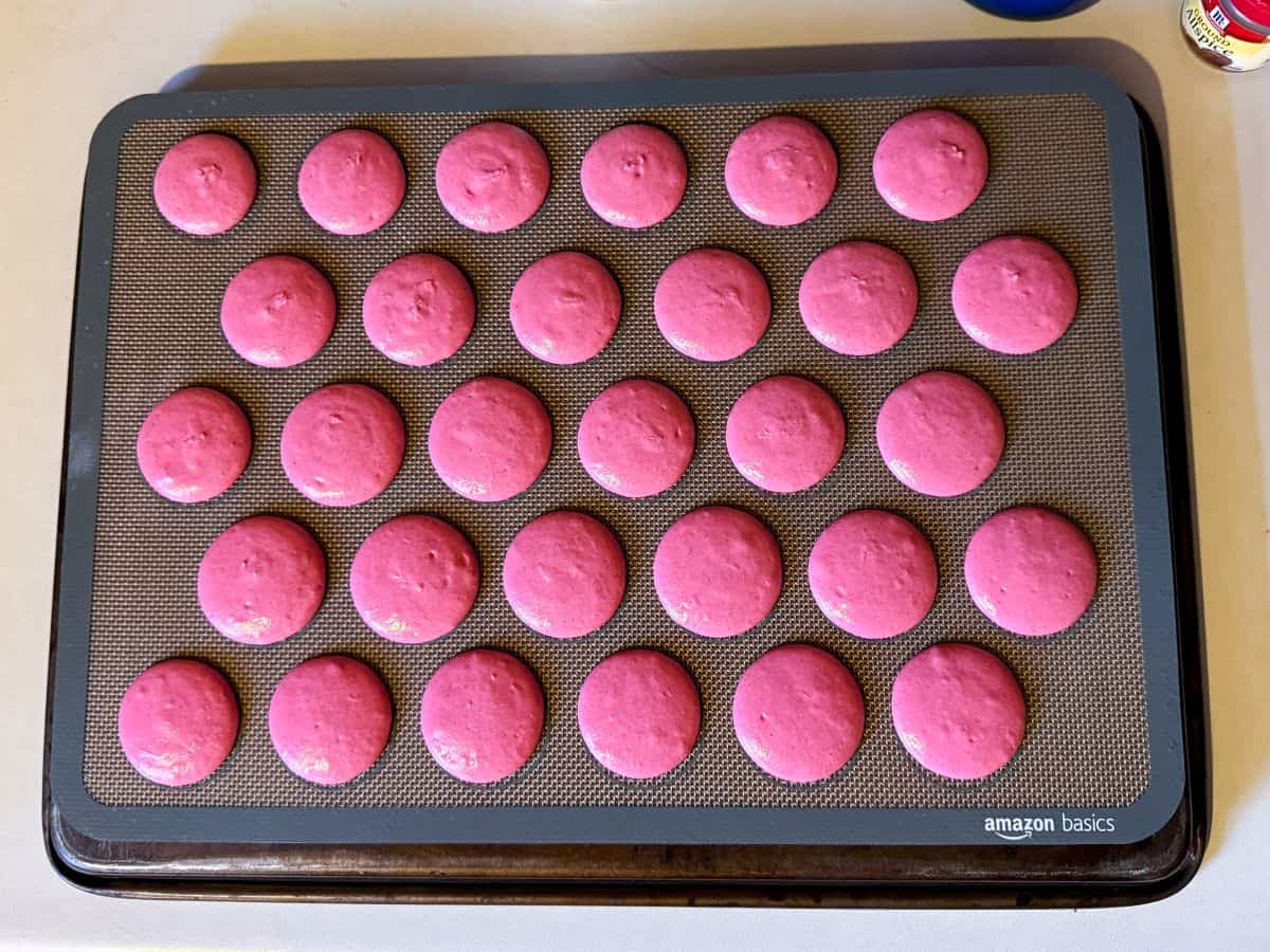 pink macaron batter piped into 1-inch circles on a macaron mat
