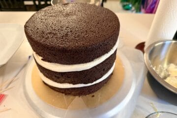3 layers of chocolate cake stacked up on a cake board before being crumb coated