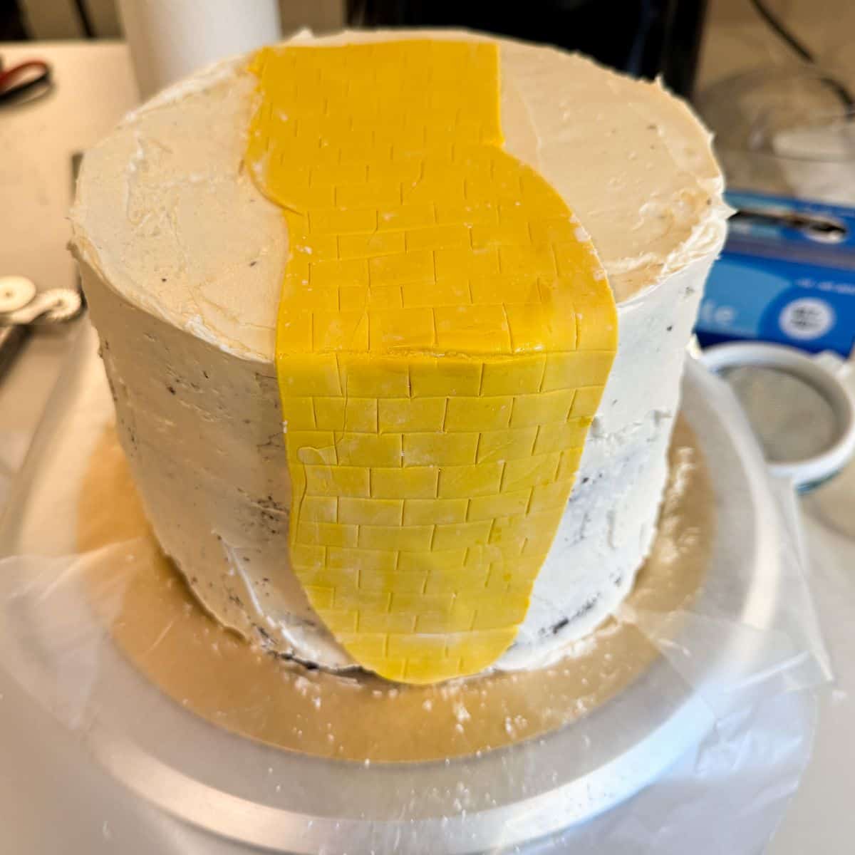 a yellow fondant brick road placed on the top and side of a round white buttercream cake