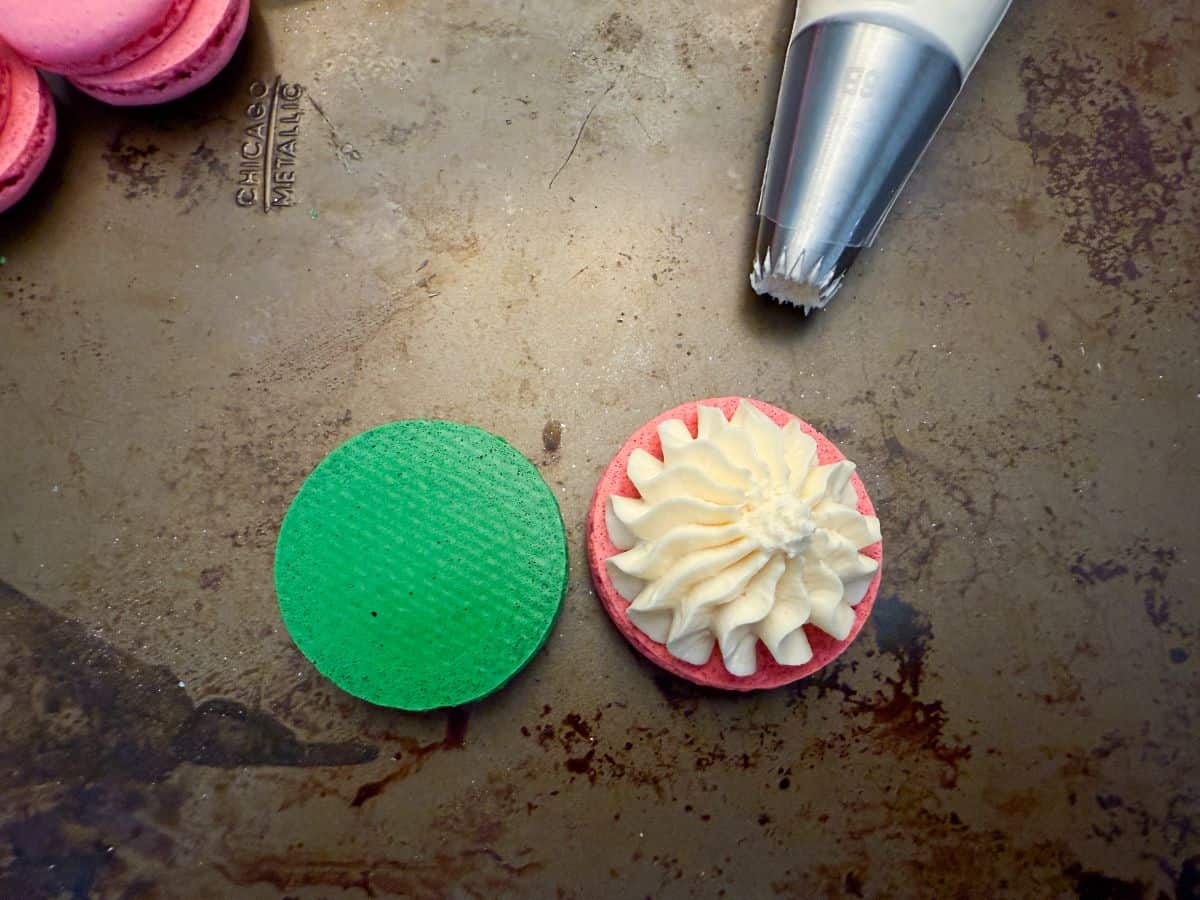 vanilla buttercream piped on top of a pink macaron shell next to a green shell