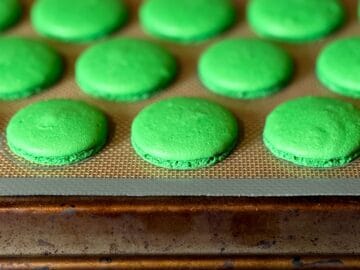 baked green macaron shells on a macaron mat