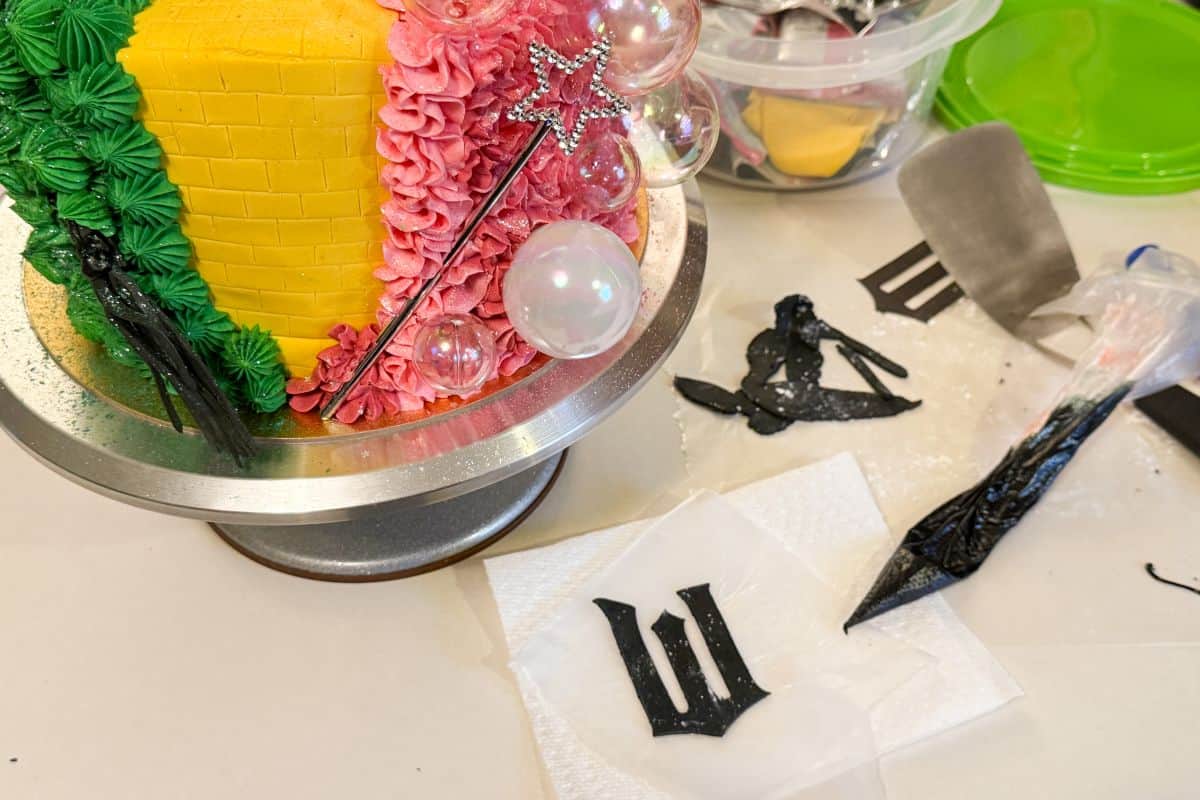 a black fondant W in the Wicked font next to a Wicked cake