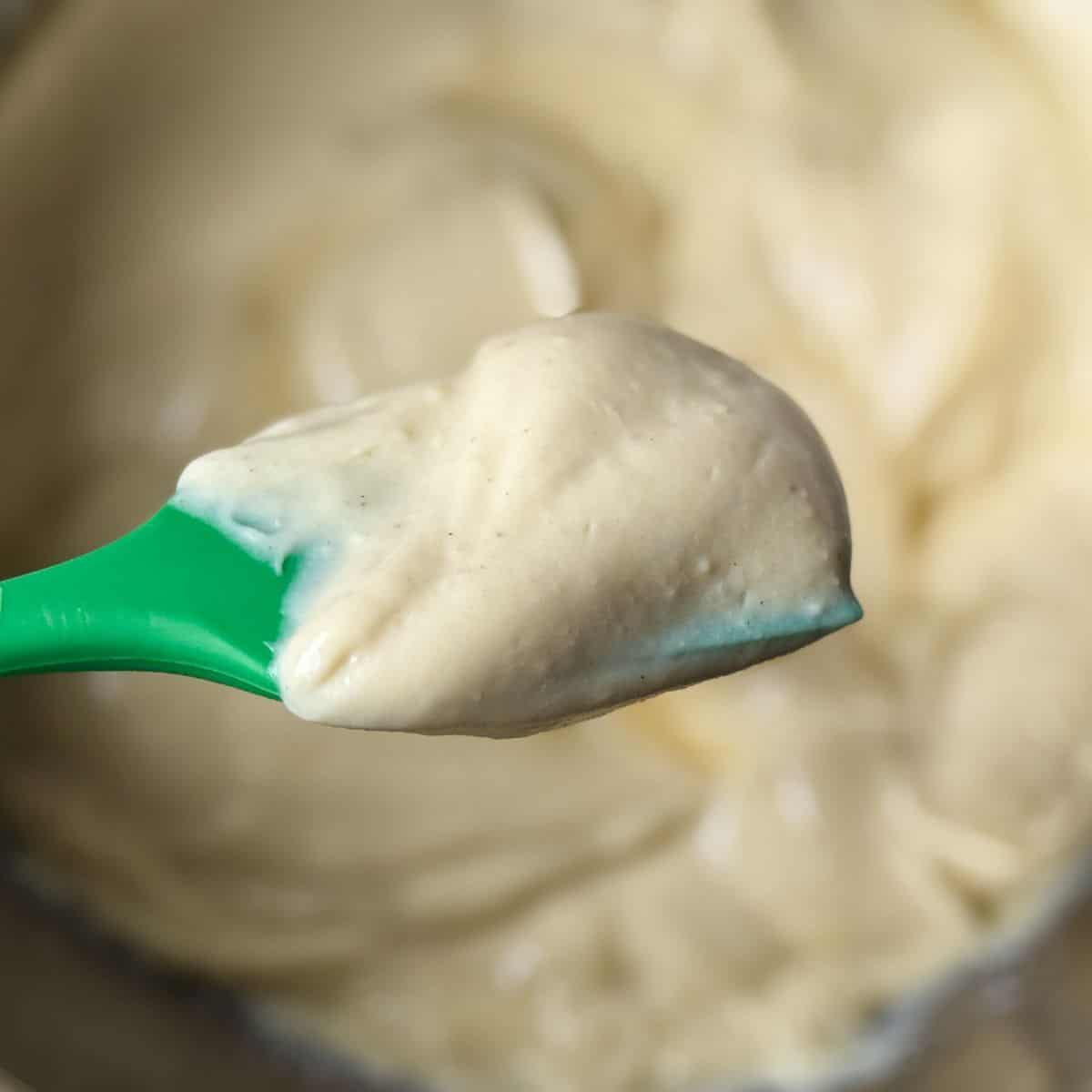 Eggnog Pastry Cream on a green silicone spatula held over a bowl with the cream
