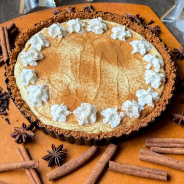 an eggnog tart with gingersnap crust on a cutting board with cinnamon sticks and star anise around it