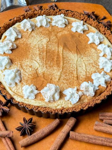 an eggnog tart with gingersnap crust on a cutting board with cinnamon sticks and star anise around it