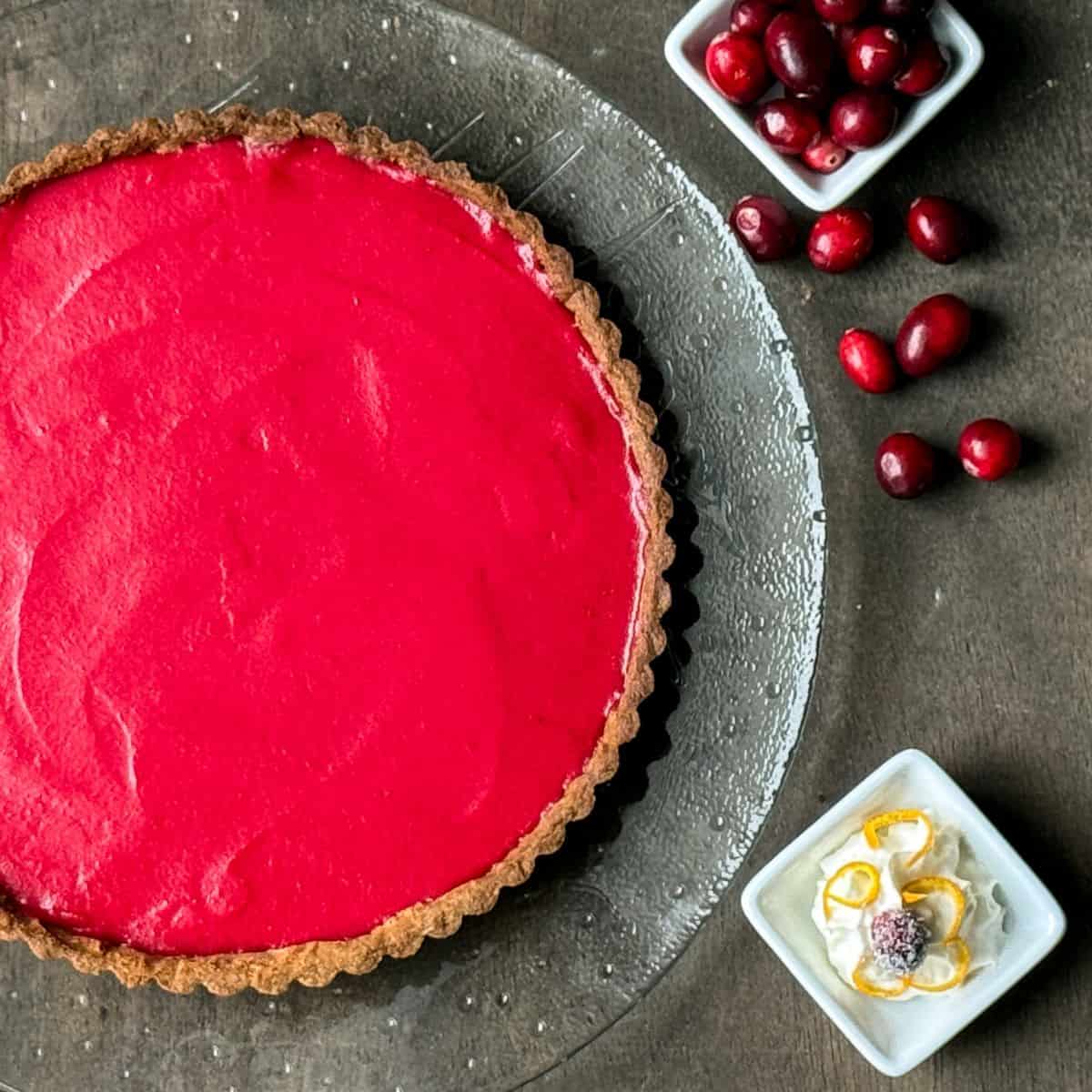 cranberry curd tart taken from above with a dish of fresh cranberries and a dish of whipped cream