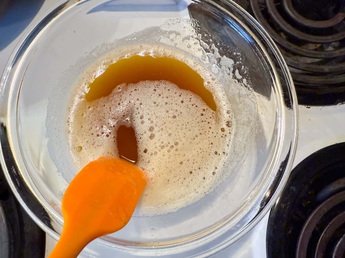 a glass bowl filled with browned butter and an orange small silicone spatula