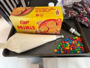 a box of Eggos Minis next to a piping bag with vanilla buttercream and a pile of M&M's