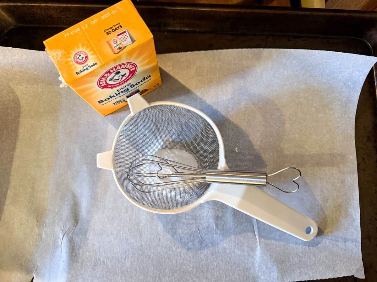 a small wire strainer with a wire whisk inside on a piece of parchment next to a box of baking soda
