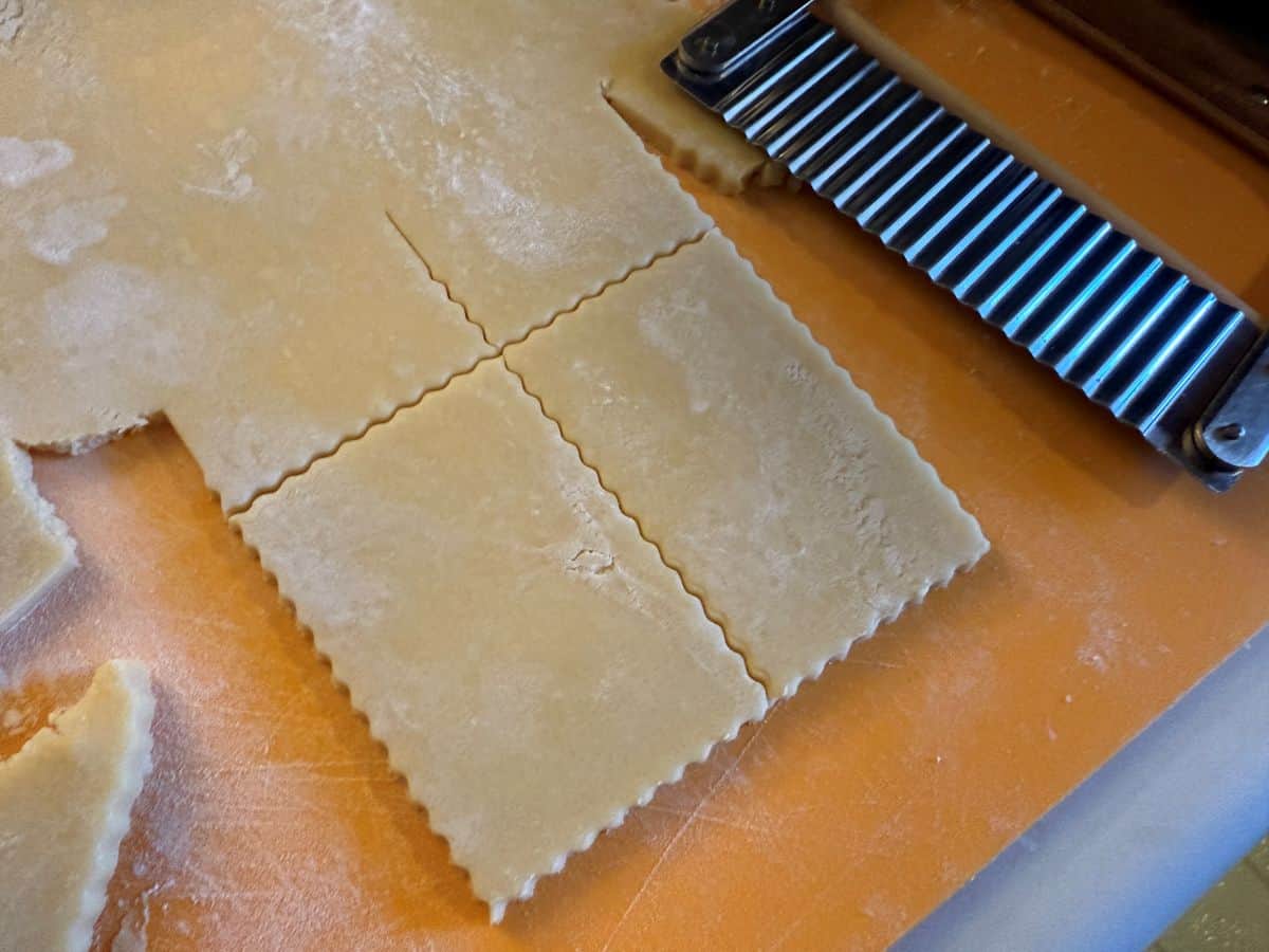 sugar cookie dough rolled out on a mat and cut with a straight scalloped edge