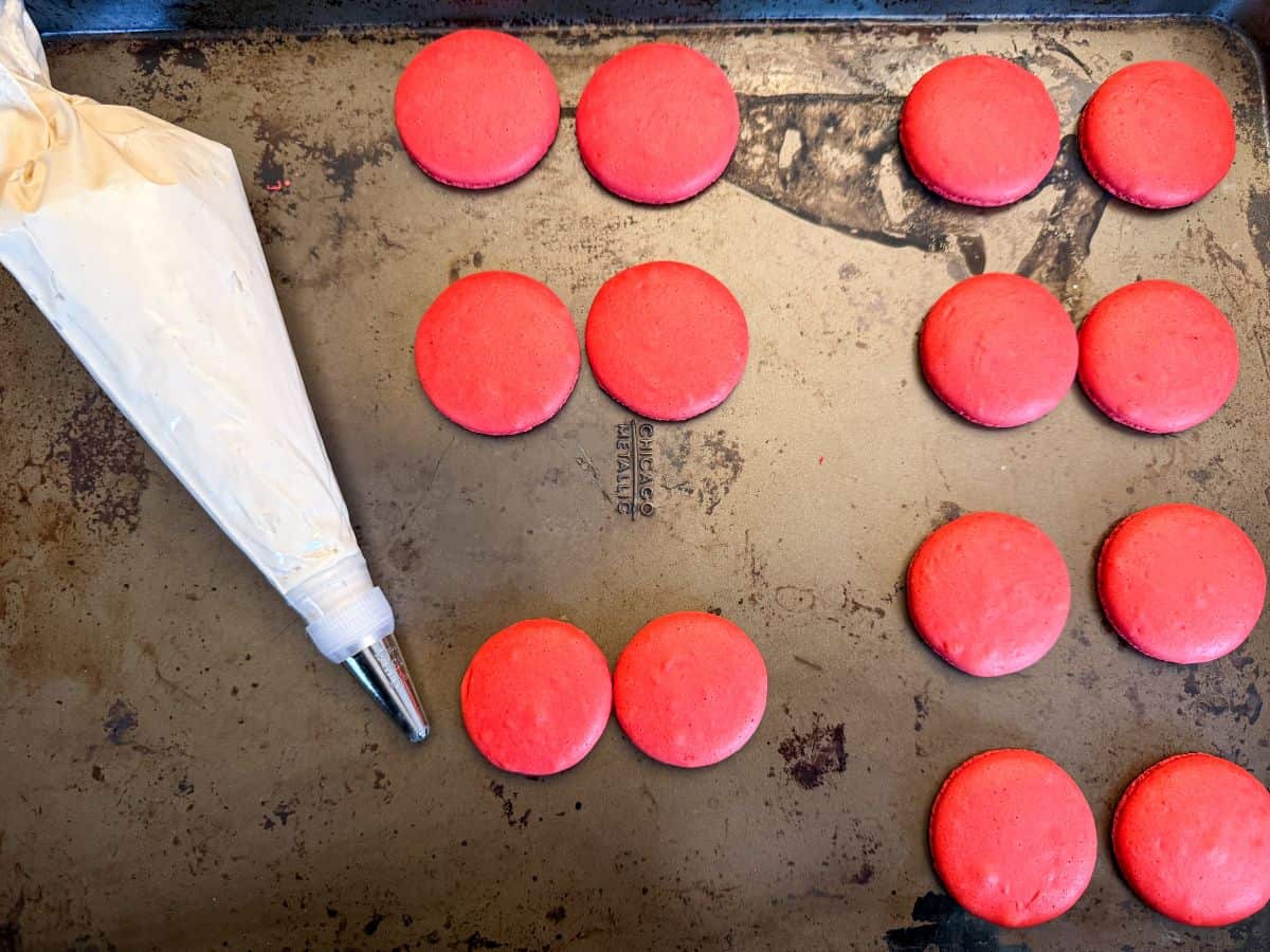 red macaron shells with a piping bag filled with easy coffee buttercream