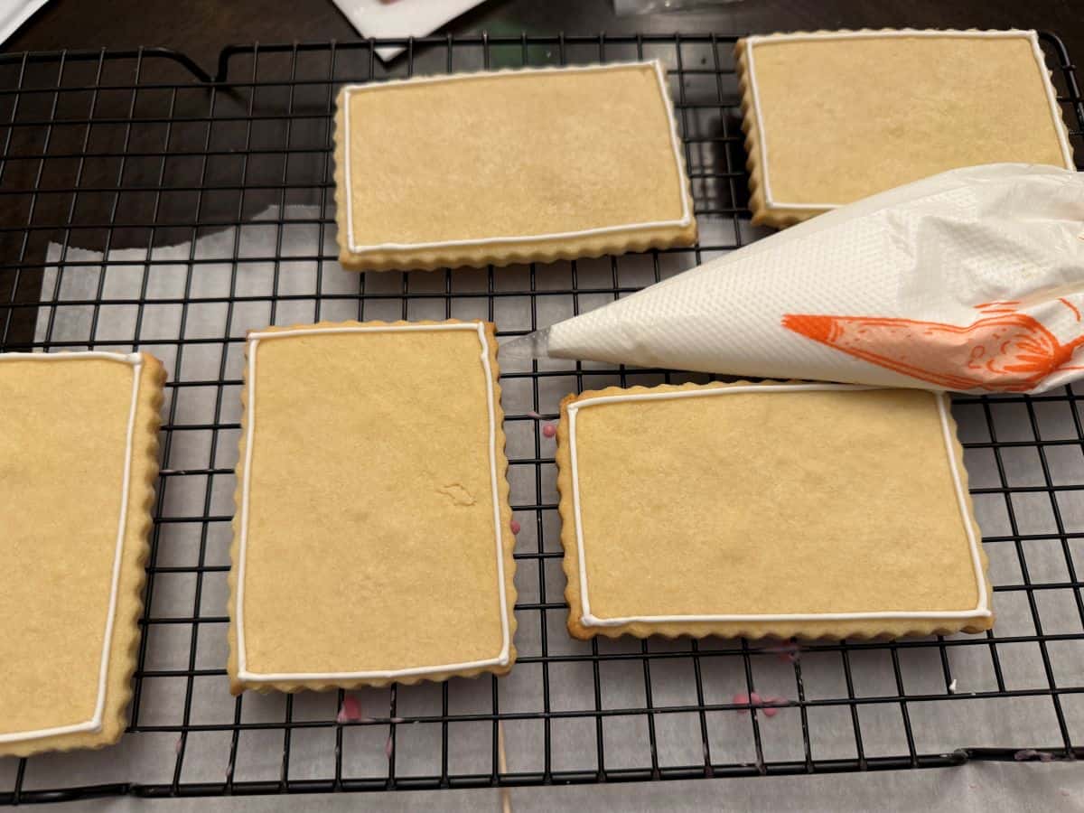 sugar cookies outlined in white royal icing on a cooling rack with a piping bag filled with white royal icing